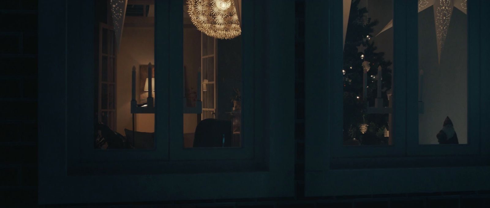 A house at night, cool and blue, lit windows beyond