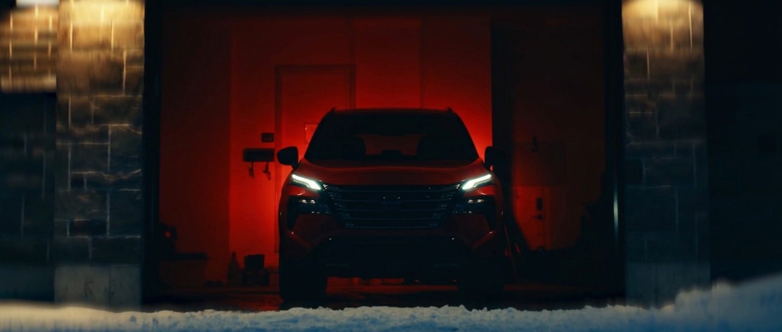 A garage washed in red light, headlights burning through falling snow