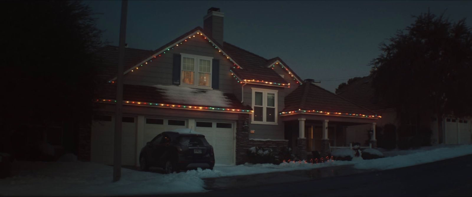 A house at night with holiday lights and a vehicle in the driveway