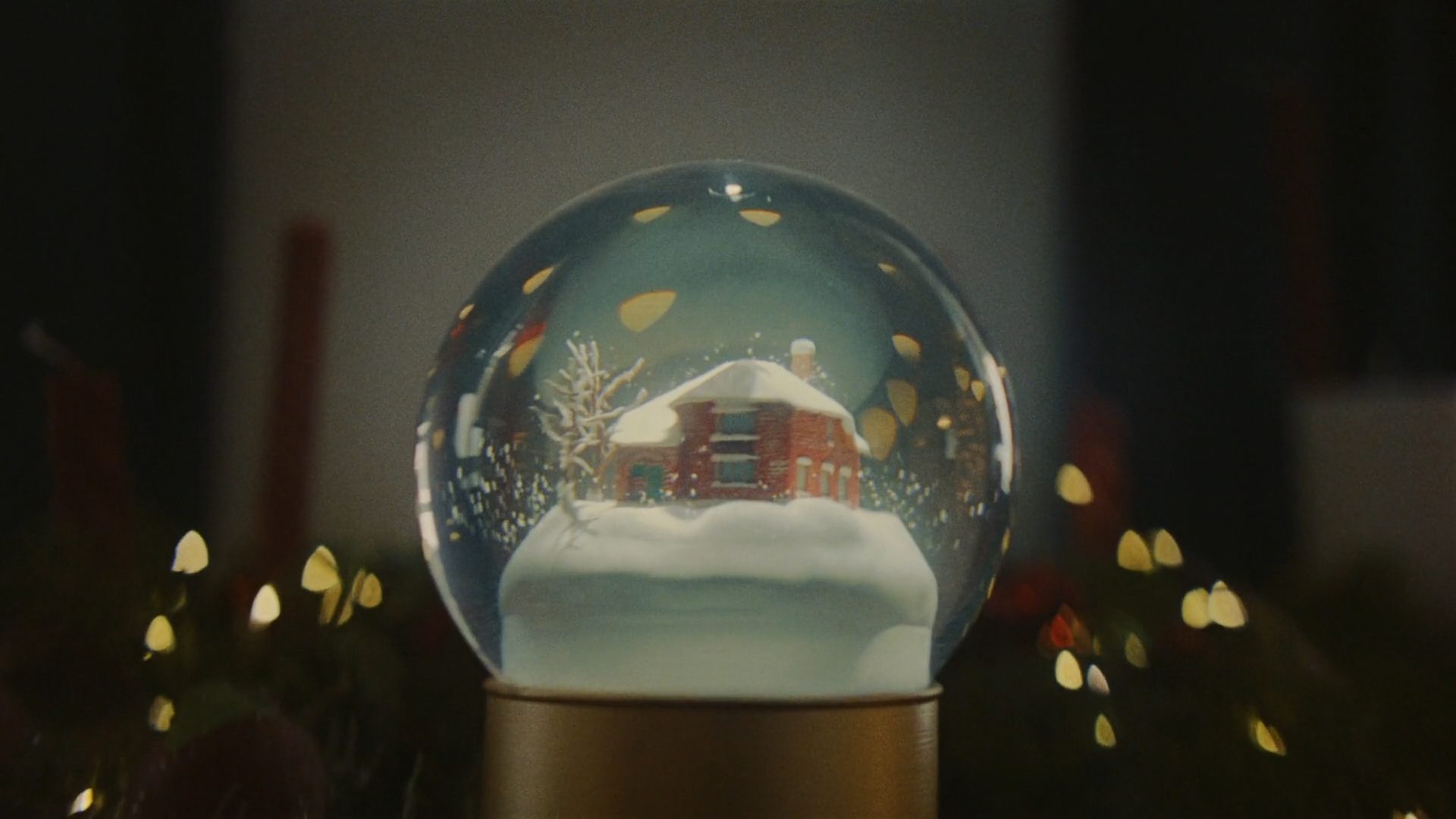 A snow globe holding a lit house, foreground lights thrown soft